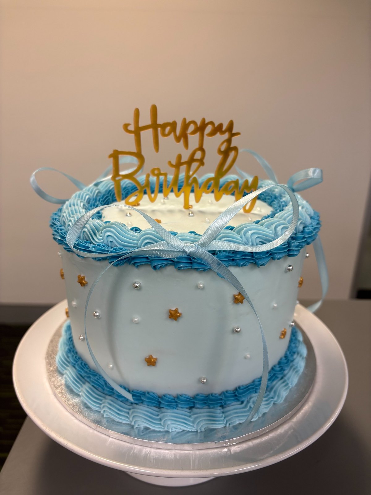 Blue piped birthday cake with bows, pearls and gold stars